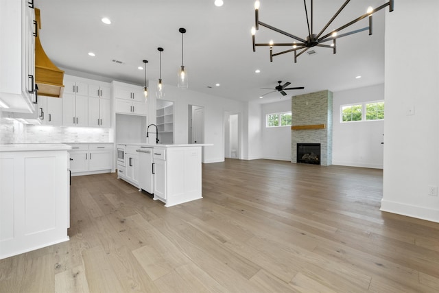 kitchen featuring white cabinetry, decorative light fixtures, light hardwood / wood-style floors, and a center island with sink