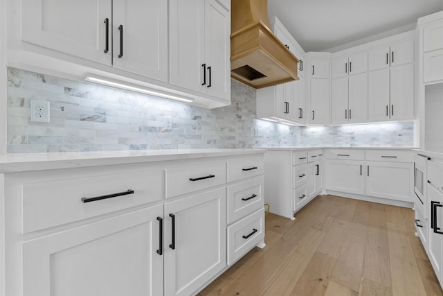 kitchen with tasteful backsplash, premium range hood, white cabinetry, and light hardwood / wood-style floors