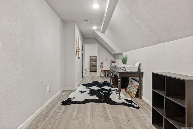 interior space featuring vaulted ceiling, light wood-type flooring, and a textured ceiling