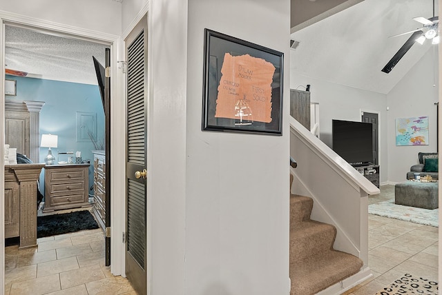 staircase with lofted ceiling, a textured ceiling, tile patterned floors, and ceiling fan