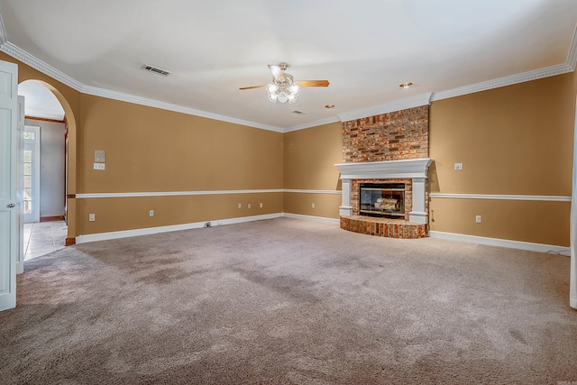 unfurnished living room with crown molding, carpet, ceiling fan, and a brick fireplace