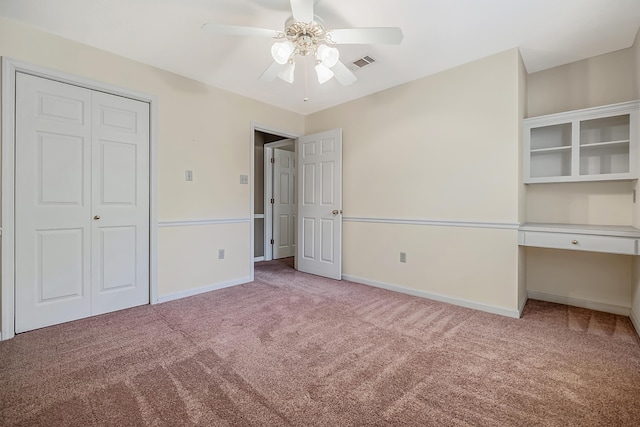 unfurnished bedroom featuring built in desk, light carpet, ceiling fan, and a closet