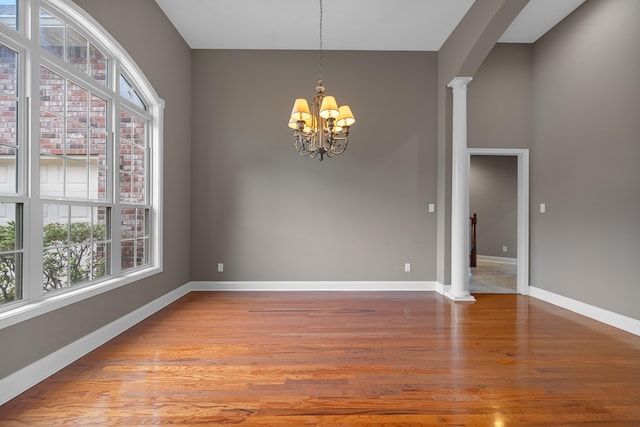 empty room featuring an inviting chandelier, wood-type flooring, and ornate columns