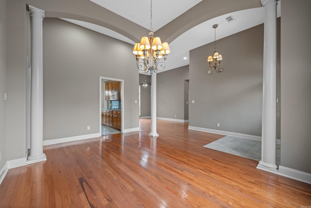 unfurnished dining area with a notable chandelier, wood-type flooring, and decorative columns