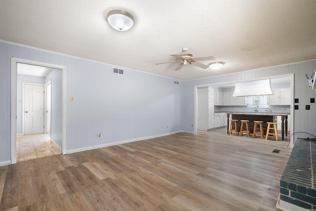 unfurnished living room with ceiling fan, light hardwood / wood-style floors, and ornamental molding