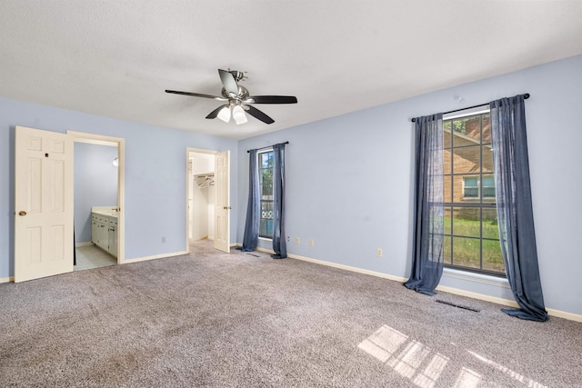 unfurnished bedroom featuring multiple windows, light carpet, a walk in closet, and ceiling fan