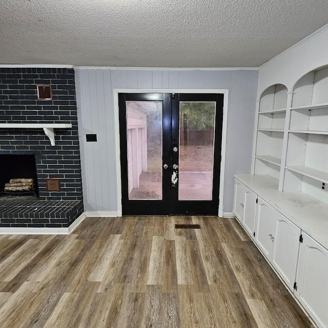 unfurnished living room featuring french doors, brick wall, a textured ceiling, wood-type flooring, and a brick fireplace