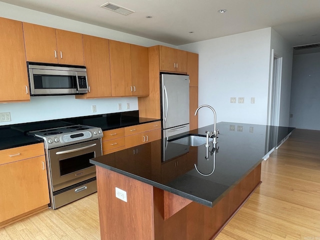 kitchen with light hardwood / wood-style floors, sink, appliances with stainless steel finishes, and a center island with sink