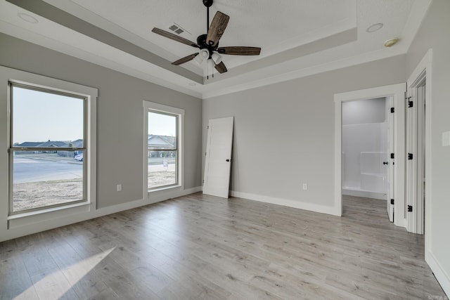 empty room with light hardwood / wood-style flooring, a raised ceiling, and ceiling fan