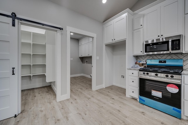 kitchen with a barn door, appliances with stainless steel finishes, white cabinets, and decorative backsplash