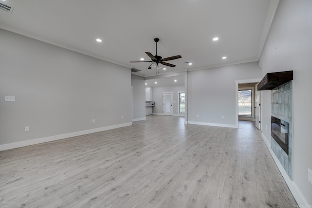 unfurnished living room featuring crown molding, ceiling fan, a tiled fireplace, and light hardwood / wood-style flooring