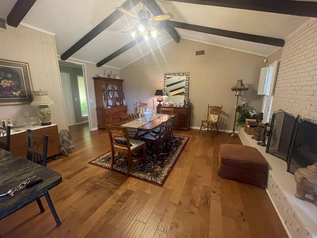 dining room featuring a brick fireplace, hardwood / wood-style flooring, lofted ceiling with beams, and ceiling fan