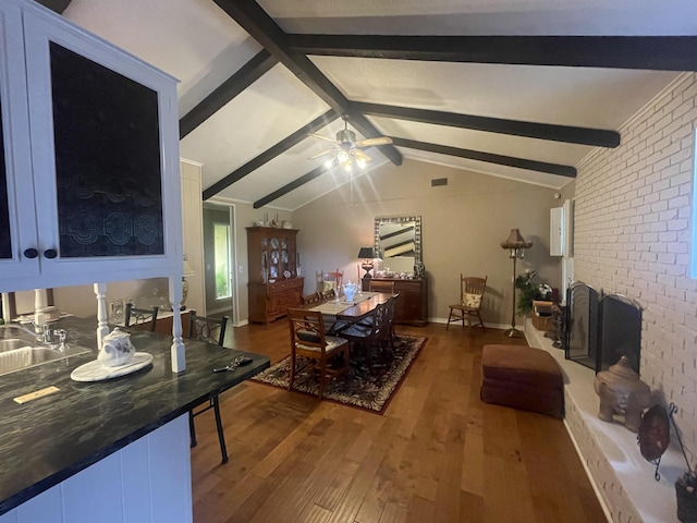 living room featuring sink, ceiling fan, hardwood / wood-style floors, lofted ceiling with beams, and a brick fireplace