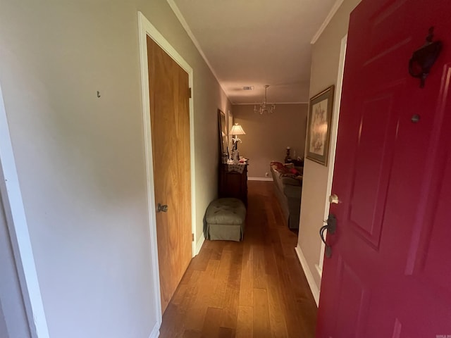 hallway with an inviting chandelier, wood-type flooring, and ornamental molding