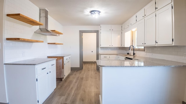 kitchen featuring sink, wall chimney range hood, kitchen peninsula, and white cabinets