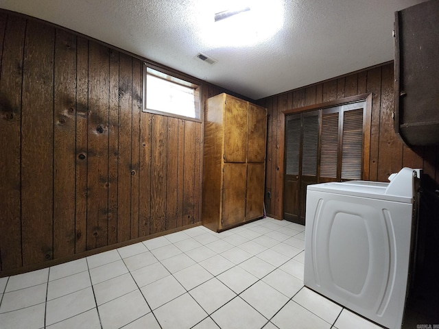 clothes washing area with washer / dryer, a textured ceiling, light tile patterned floors, and wooden walls