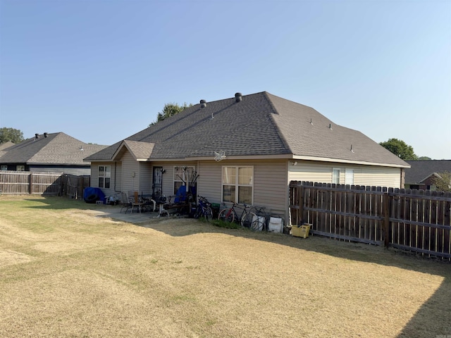 back of property featuring a patio, a shingled roof, a lawn, and a fenced backyard