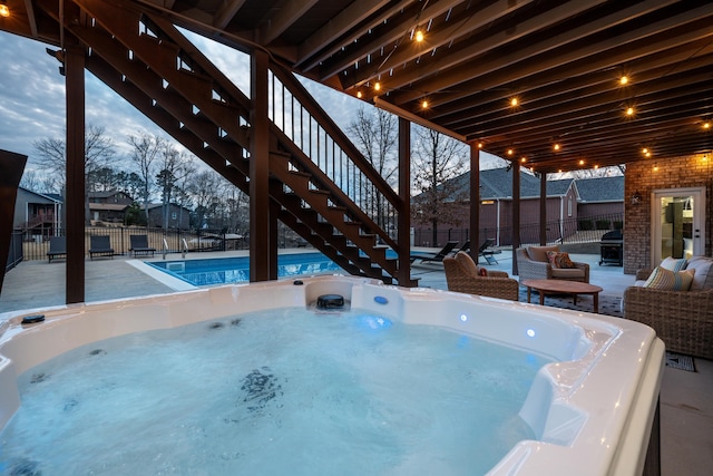 pool at dusk with a hot tub and a patio