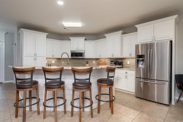 kitchen featuring stainless steel appliances, a kitchen island with sink, white cabinets, and backsplash