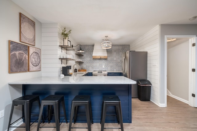 kitchen featuring premium range hood, appliances with stainless steel finishes, a kitchen breakfast bar, kitchen peninsula, and light hardwood / wood-style floors