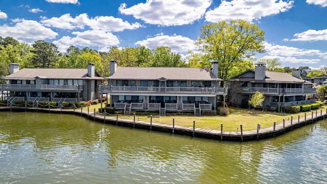 back of property featuring a balcony, a water view, and a lawn