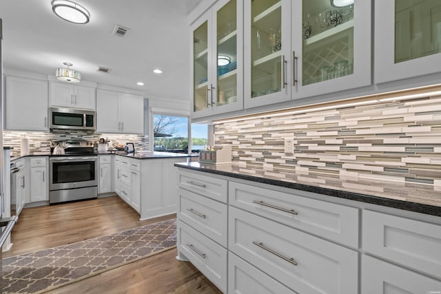 kitchen with stainless steel appliances, white cabinets, glass insert cabinets, and dark stone countertops