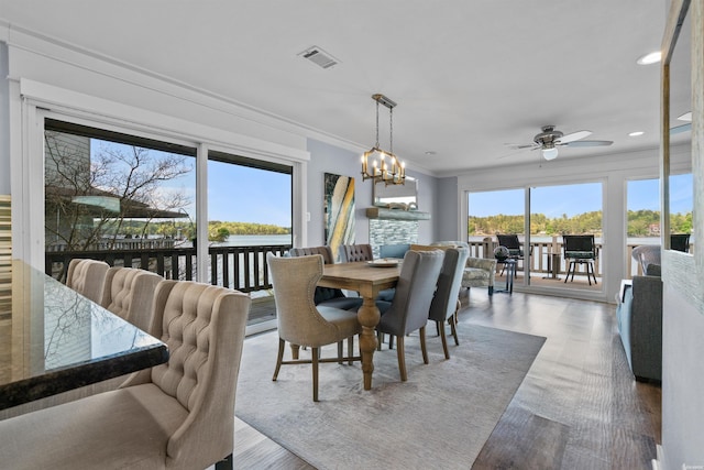 dining area featuring visible vents, ornamental molding, wood finished floors, a water view, and ceiling fan with notable chandelier