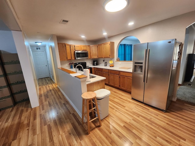 kitchen featuring sink, light hardwood / wood-style flooring, appliances with stainless steel finishes, a kitchen breakfast bar, and kitchen peninsula