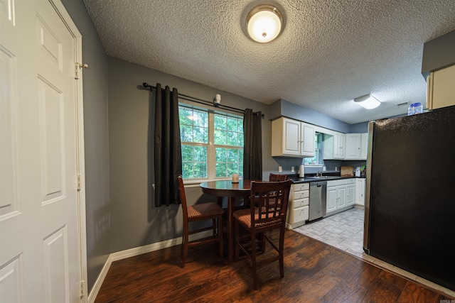 kitchen with a textured ceiling, white cabinets, fridge, stainless steel dishwasher, and tile patterned floors