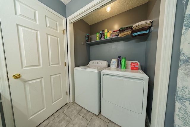 clothes washing area with washing machine and dryer, a textured ceiling, and light tile patterned floors