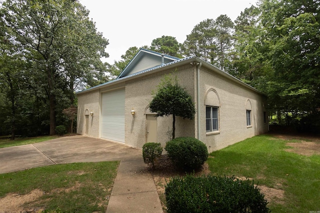 view of side of property with a garage, driveway, brick siding, and a lawn