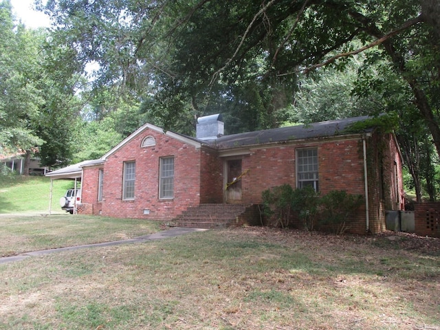 ranch-style home featuring an attached carport, brick siding, a chimney, and a front yard