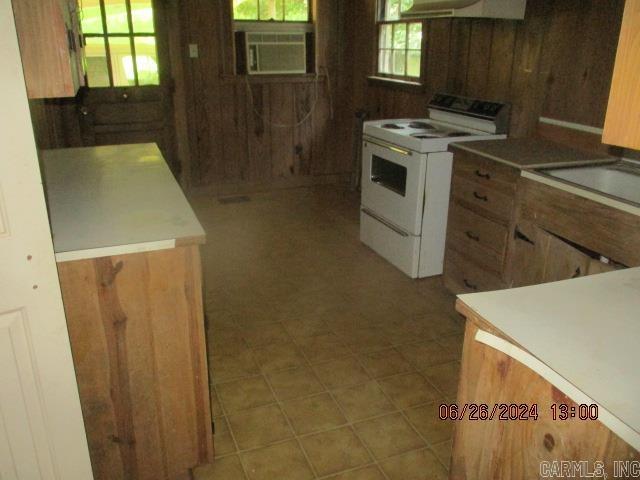 kitchen with white electric range oven, ventilation hood, cooling unit, and wood walls