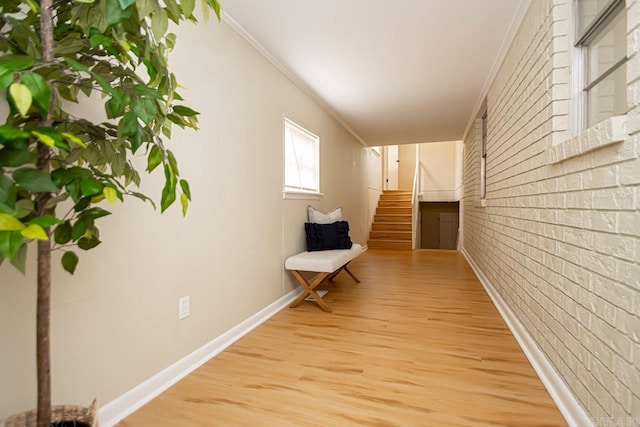 hall featuring crown molding, brick wall, and light wood-type flooring