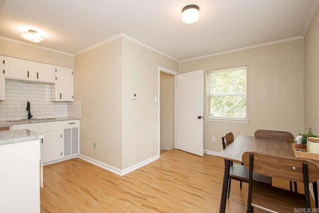 kitchen with white cabinets, sink, backsplash, light wood-type flooring, and light stone countertops