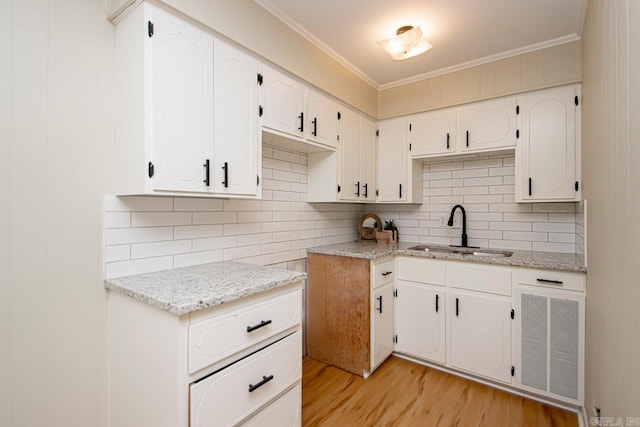 kitchen featuring white cabinets, sink, light stone counters, light hardwood / wood-style floors, and decorative backsplash