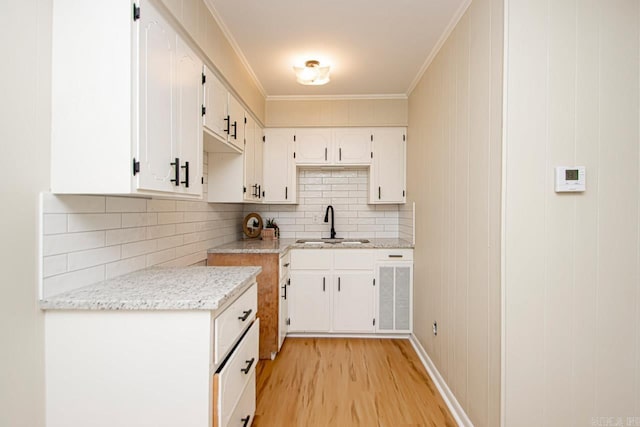 kitchen featuring white cabinetry, crown molding, light hardwood / wood-style flooring, light stone countertops, and sink