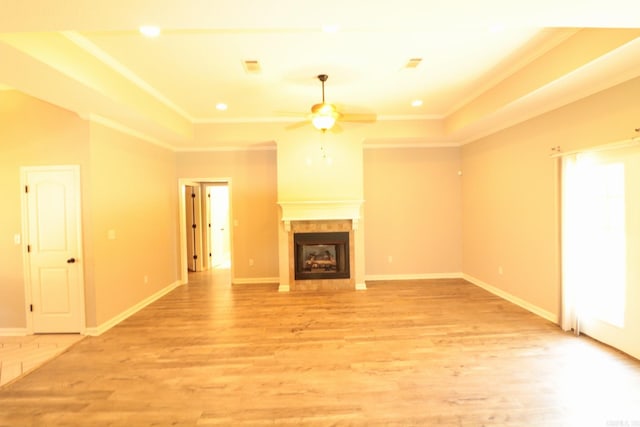 unfurnished living room with crown molding, a tile fireplace, light hardwood / wood-style flooring, and ceiling fan