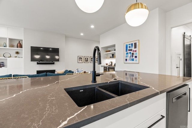 kitchen featuring dark stone counters, pendant lighting, built in features, sink, and dishwasher