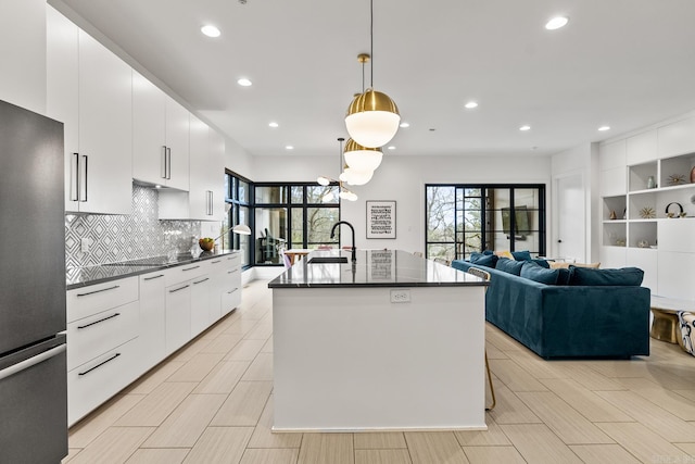 kitchen with white cabinetry, an island with sink, hanging light fixtures, decorative backsplash, and stainless steel fridge