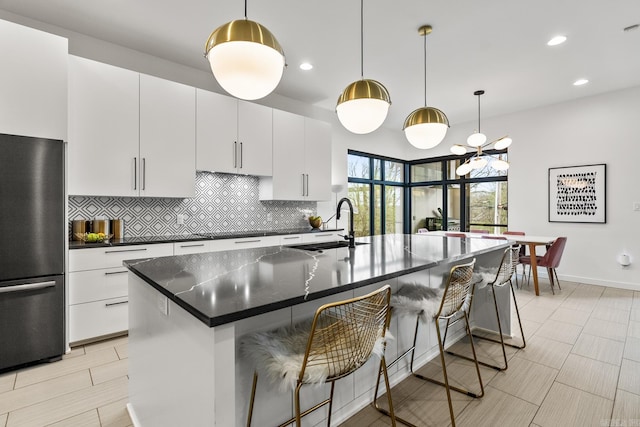 kitchen with tasteful backsplash, decorative light fixtures, black fridge, and a center island with sink