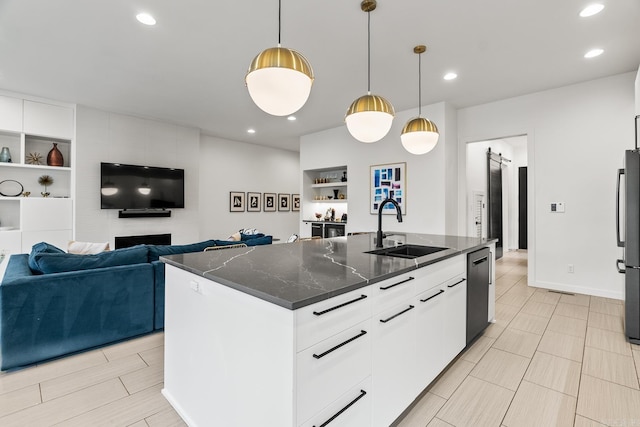 kitchen with white cabinets, dark stone counters, sink, and an island with sink