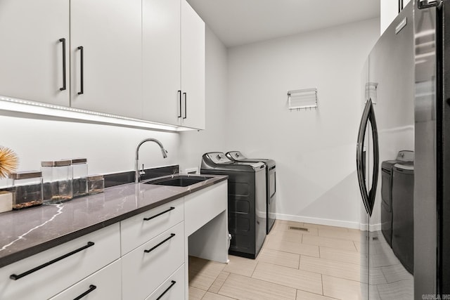 clothes washing area featuring light tile patterned flooring, cabinets, washing machine and dryer, and sink