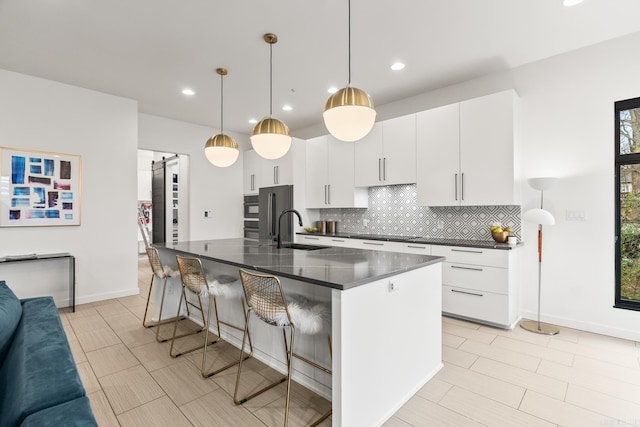 kitchen featuring tasteful backsplash, white cabinets, a center island with sink, a breakfast bar, and sink