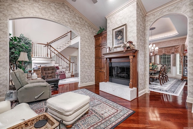 living room featuring wood finished floors, arched walkways, crown molding, a chandelier, and stairs