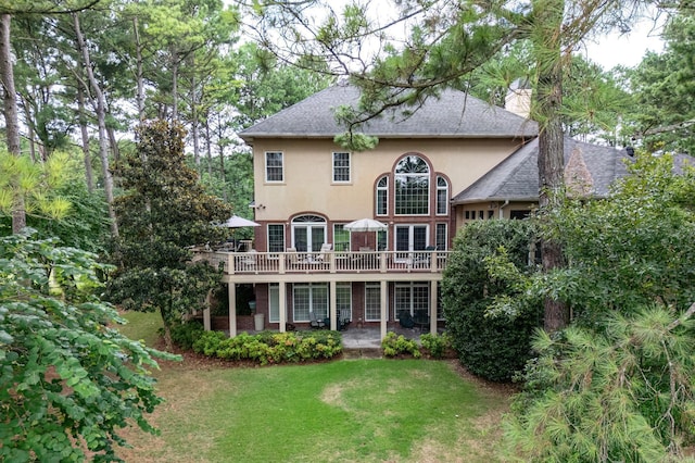 rear view of property featuring roof with shingles, a wooden deck, a yard, stucco siding, and brick siding