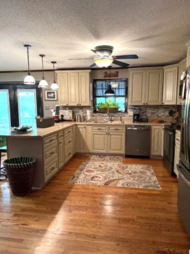 kitchen with pendant lighting, sink, stainless steel refrigerator, dishwasher, and light wood-type flooring