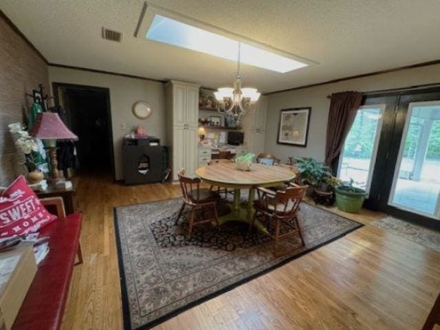 dining area featuring ornamental molding, a textured ceiling, a notable chandelier, and light wood-type flooring