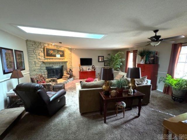 living room with ceiling fan, a stone fireplace, and dark carpet