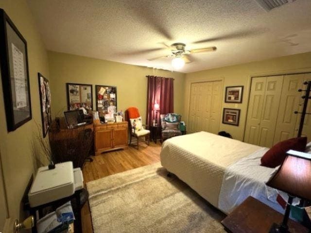 bedroom featuring multiple closets, ceiling fan, light hardwood / wood-style floors, and a textured ceiling